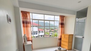 A bedroom with a large bed, a wooden wardrobe, a desk with a chair, a window with curtains, and a view of buildings and hills outside. - Amazing 4-bedroom third floor apartment in San Ramón (San Ramón)
