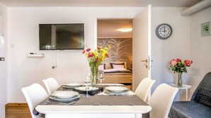A dining area with a table set for four, a TV mounted on the wall, and a clock on the wall. - Adelsberg Inn by Interhome (Postojna)