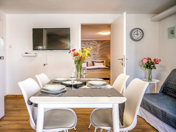 Un coin repas avec une table dressée pour quatre personnes, un téléviseur fixé au mur et une horloge également accrochée au mur.