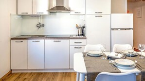 A modern kitchen with white cabinets, a stainless steel range hood, and a dining area set for four with a table, chairs, and dinnerware. - Adelsberg Inn by Interhome (Postojna)