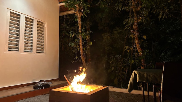 A small outdoor fire feature with a brick base, surrounded by a paved area and a white building with windows.