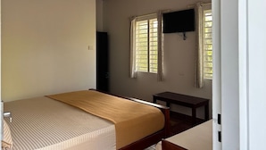 A room with a bed, a ceiling fan, a TV mounted on the wall, and two windows with curtains.