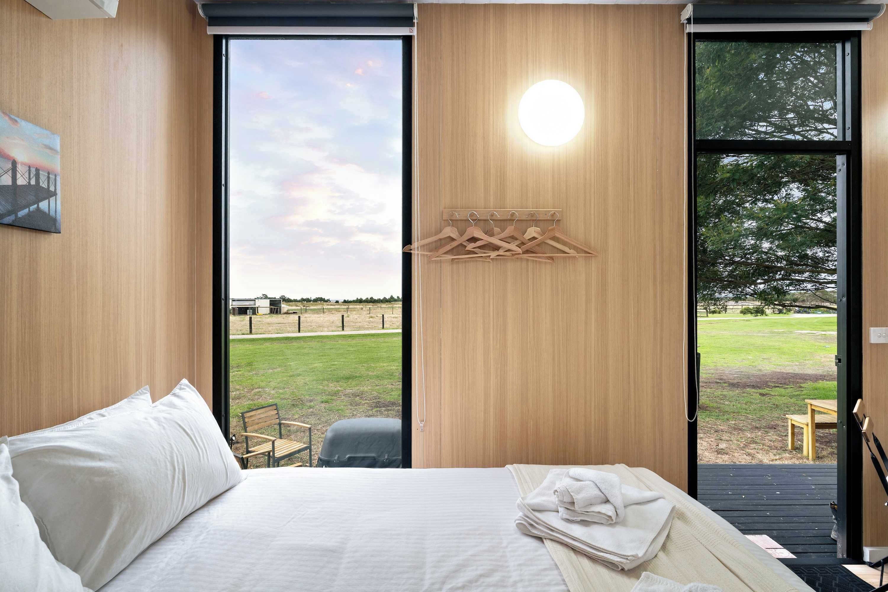 Une chambre à coucher avec un lit, un mur en bois, une fenêtre et une vue sur un champ verdoyant.