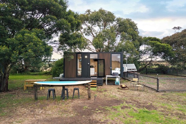 A modern outdoor living area with a pool table, seating, and a small building with a deck.