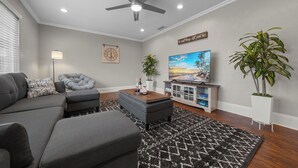 A living room with a gray sofa, a gray armchair, a wooden coffee table, a TV, a ceiling fan, and a wall clock.