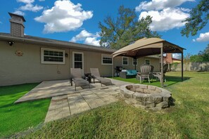 A backyard with a covered patio, outdoor seating, and a fire pit.
