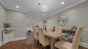 A dining area with a wooden table, beige upholstered chairs, a chandelier, and a decorative mirror on the wall.