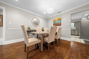 A dining area with a round table and four chairs, a chandelier, a mirror, and a painting on the wall.