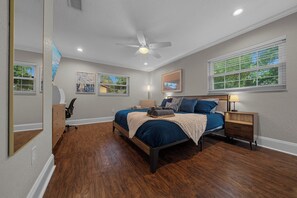 A bedroom with a bed, a desk, a chair, a nightstand, and a window.