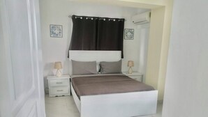 Une chambre à coucher comprenant un lit, deux tables de chevet, une commode, une fenêtre avec des rideaux et un appareil de climatisation.
