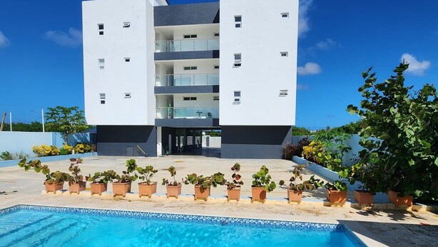 Un bâtiment moderne doté d’une piscine, de plantes en pot et surplombant un ciel bleu azur.