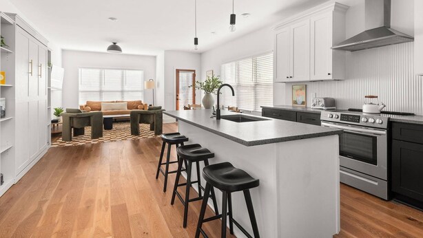 A modern kitchen with a central island, bar stools, a dining area with a sofa, and a large window with blinds. - CP ~ Hot Tub ~ Outdoor Lounge & TV ~ Walkable to Local Food & Drinks ~ Free Parking ~ Sleeps 10 (Nashville)