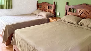 Una stanza con due letti singoli e un letto più grande, con testiere in legno, una parete verde e una lampada a soffitto.