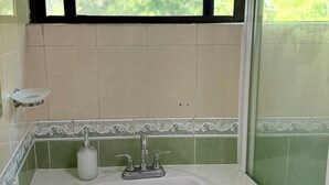 Un bagno con un lavandino bianco, piastrelle verdi e una finestra vista sul verde.