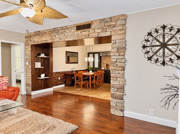 A dining area with a stone wall, wooden furniture, and a ceiling fan.