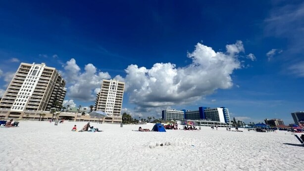 Une plage avec de grands immeubles en arrière-plan, du sable fin et un ciel dégagé.