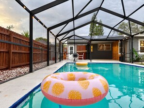 An outdoor swimming pool with a covered area, surrounded by a wooden fence and a house in the background. - Sunny Clearwater Escape | 3BR + Pool + 3 Baths (Clearwater)