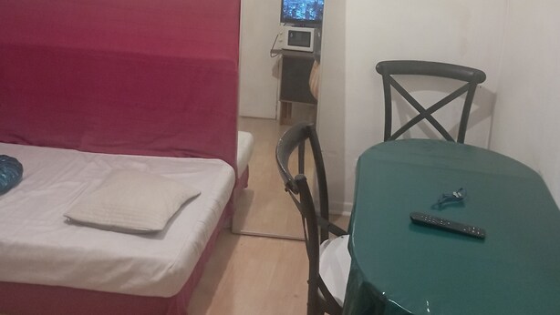 A small room with a bed, a table, and a chair. There is a television on a shelf above the bed.
