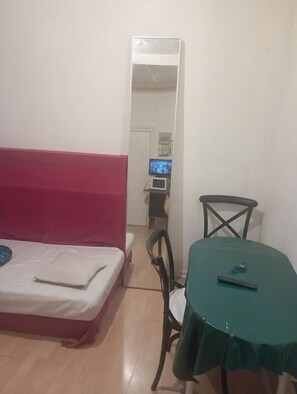Habitació petita amb un llit, una taula i una cadira. Hi ha un televisor sobre una estanteta a sobre del llit.