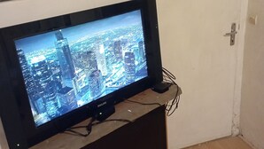 A television on a wooden stand in a room with a white door and a wall-mounted electrical box.