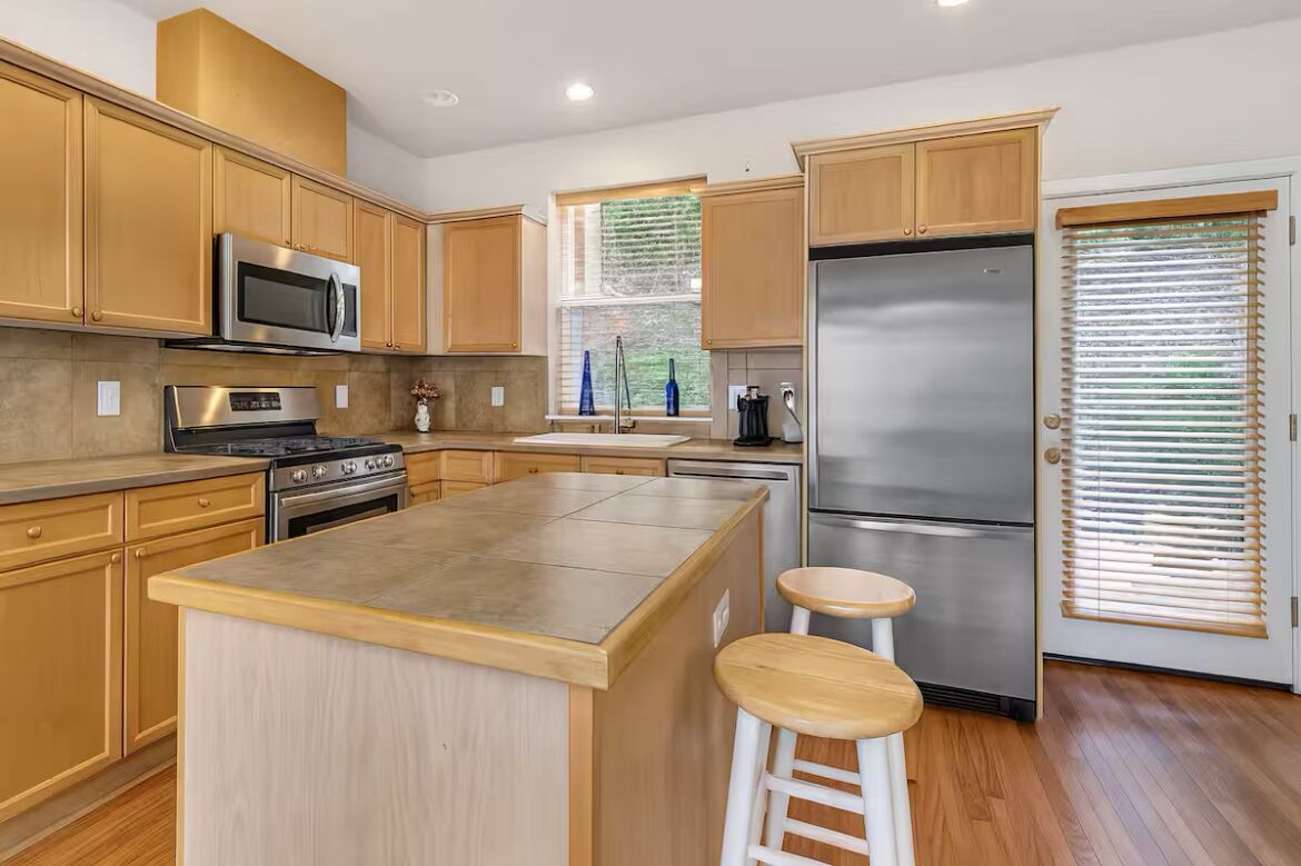A modern kitchen with wooden cabinets, stainless steel appliances, and a central island with stools.
