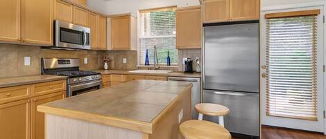 A modern kitchen with wooden cabinets, stainless steel appliances, and a central island with stools.