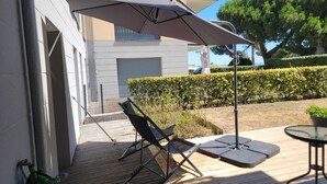 A patio with a table and chairs, a large umbrella, and a hedge. - Large apartment with private garden (Arcachon)