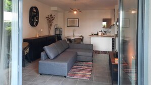A modern living room with a grey sectional sofa, a dining table, and a kitchen area with a white countertop. - Large apartment with private garden (Arcachon)