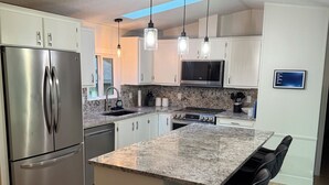 A modern kitchen with a stainless steel refrigerator, granite countertops, and pendant lighting.