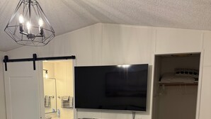 A bedroom with a bed, a TV mounted on the wall, a closet, and a bathroom visible through an open door.