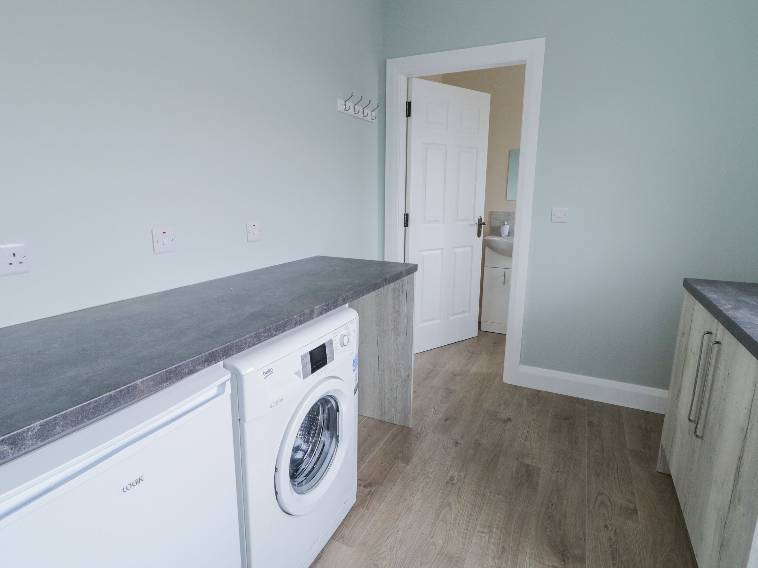 A laundry room with a washing machine, a countertop, and a door leading to a bathroom.