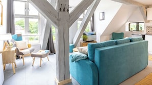 Un salon moderne doté d’un plafond haut et de poutres apparentes, d’un canapé de couleur turquoise, d’une table basse en bois et d’un téléviseur.