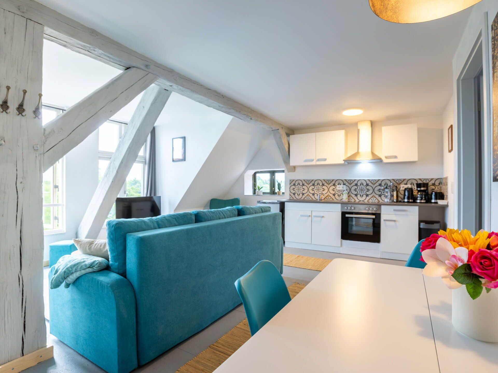 A modern kitchen with white cabinets, a tiled backsplash, and a dining area with a white table and blue chairs.