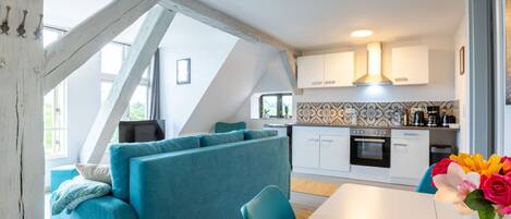 A modern kitchen with white cabinets, a tiled backsplash, and a dining area with a white table and blue chairs.