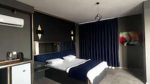 Ein Hotelzimmer mit Bett, Schreibtisch, Stuhl, Sofa, kleinem Kühlschrank und Deckenventilator.