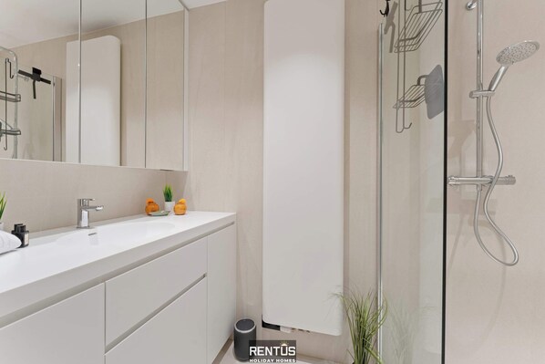 Un baño moderno con tocador blanco, cabina de ducha de vidrio y un espejo grande.