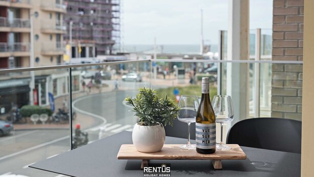 A balcony with a table, a potted plant, and a bottle of wine.