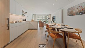 A modern kitchen with white cabinetry, a dining area with wooden chairs, and a large window providing a view of the city.