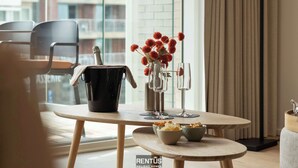 A dining area with a table set for two, a vase with red flowers, and a bowl of snacks.