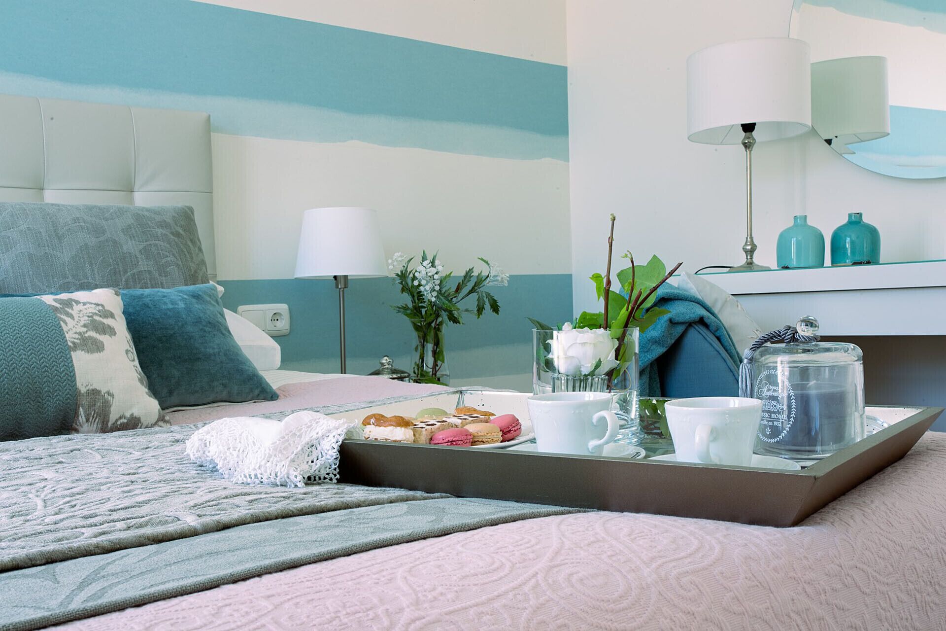 A neatly arranged bedroom with a bed, bedside table, lamp, and a tray with breakfast items.