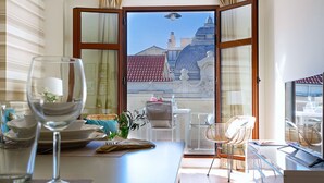 Un área de comedor con una mesa dispuesta para dos, vistas a un edificio con cúpula y un balcón con sillas de mimbre.