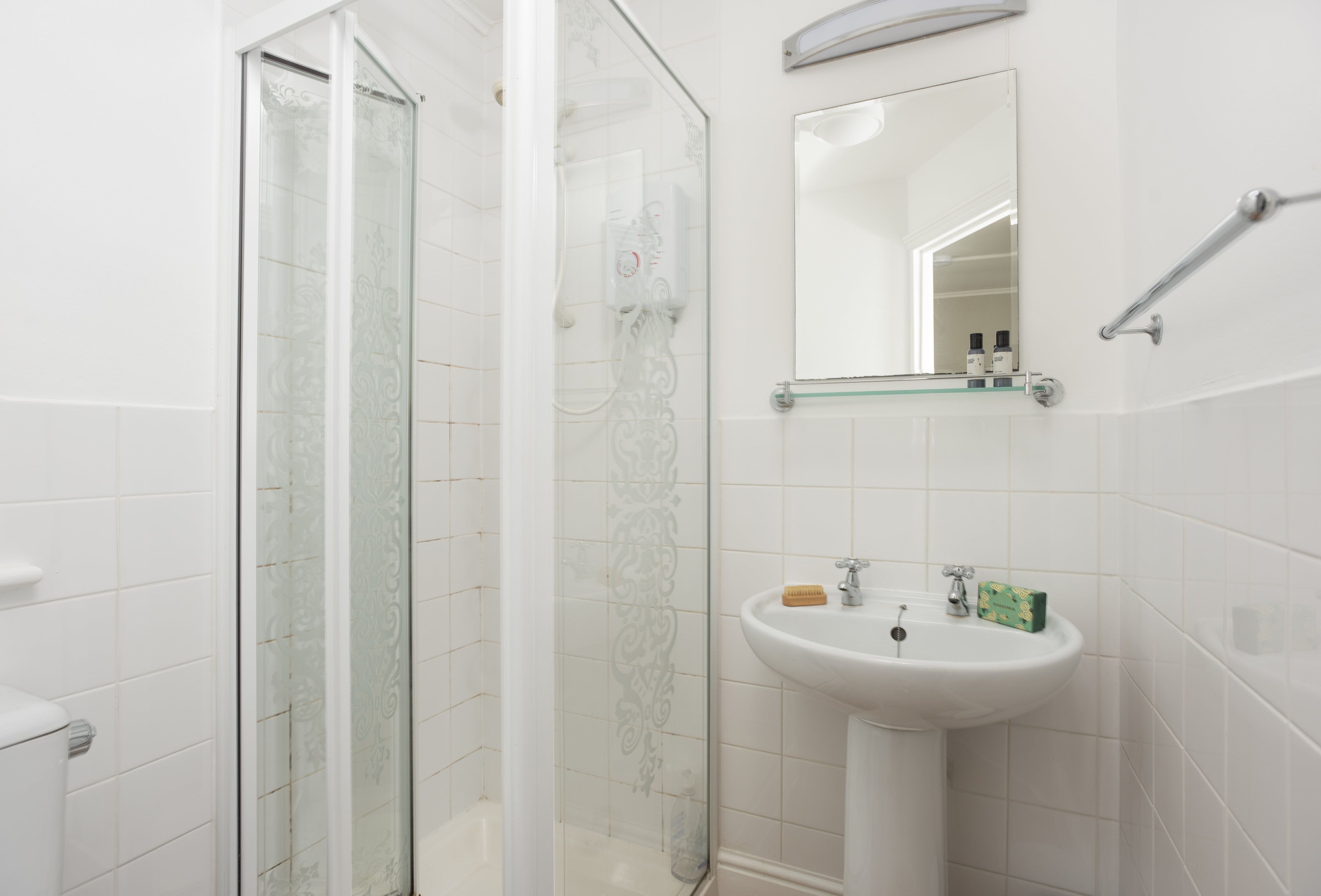 Un baño con ducha de vidrio, un lavamanos blanco con un espejo encima y un perchero para toallas.