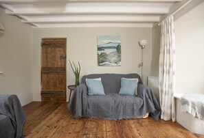 Ein Zimmer mit Holztür, einem grauen Sofa mit Kissen, einem Bild an der Wand und einer Stehlampe.
