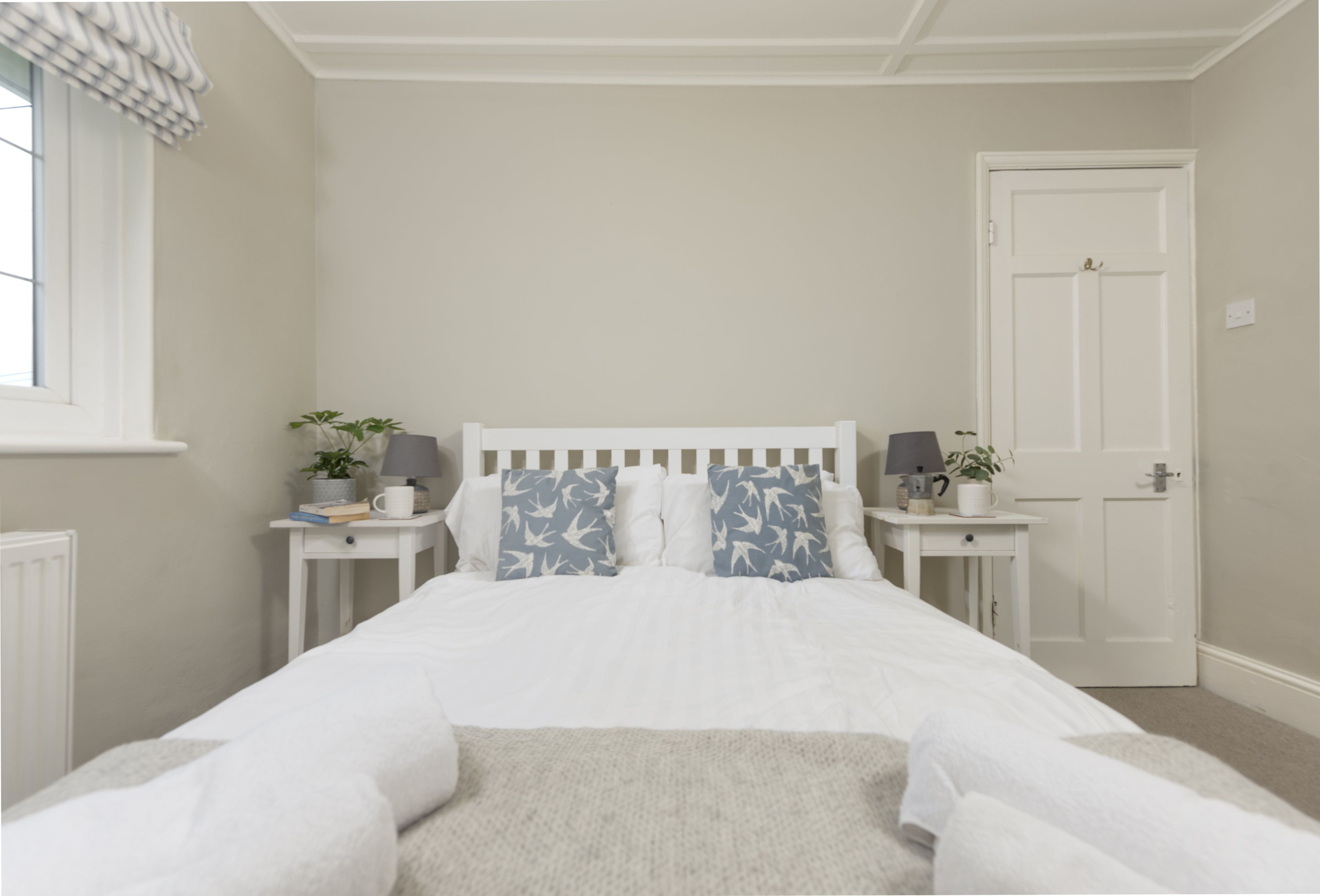 Una camera da letto con un letto bianco, due comodini, una porta e una finestra con tenda.