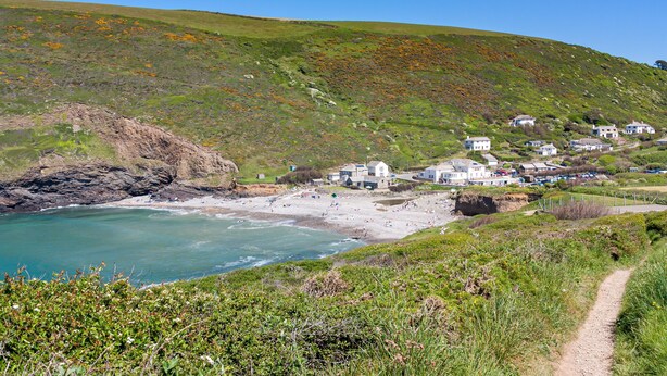 A coastal village with houses on a hillside, a sandy beach, and a clear blue sky.