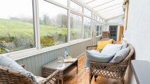 A conservatory with wicker furniture, a glass table, and a view of a green landscape.