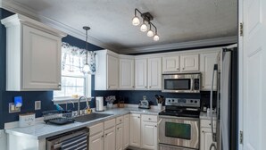 A modern kitchen with white cabinetry, stainless steel appliances, and a large island with a dishwasher. - Scenic View by the Pond in Lexington (Lexington)