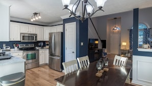A modern kitchen with stainless steel appliances, a dining area with a dark wood table, and a staircase leading to a loft. - Scenic View by the Pond in Lexington (Lexington)