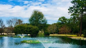 A serene lake with a fountain in the center, surrounded by lush greenery and trees.