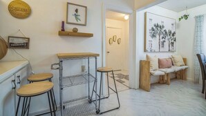 A kitchen with a metal cart, stools, and a wooden counter. There are wall decorations, a bench, and a door leading to another room.
